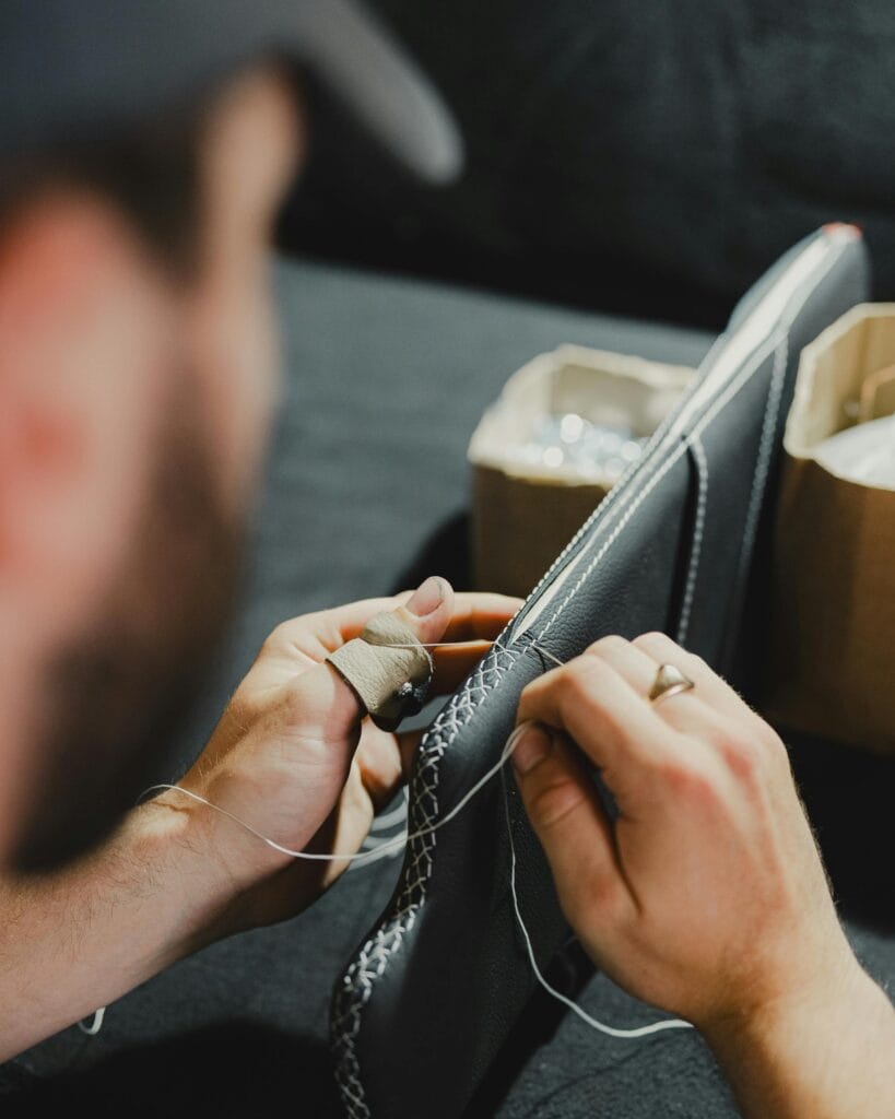 Close-up of a craftsman hand-stitching leather upholstery with precise detail.